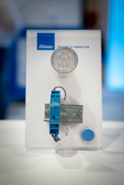 Demo panel with LED spotlight, blue DIN-rail module, and a round push button