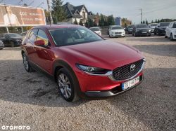 Red Mazda CX-30 car parked on a gravel lot, in the background other vehicles and a billboard.