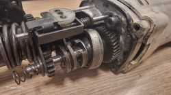 Wnętrze rozkręconej młotowiertarki z widocznymi elementami mechanicznymi, sprężynami i kołami zębatymi.