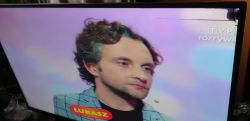 Telewizor z wyświetlanym fragmentem programu rozrywkowego z osobą o imieniu Łukasz.