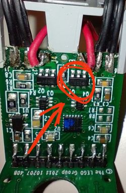 Zbliżenie na płytkę drukowaną z elektroniką i uszkodzonym elementem, zaznaczonym czerwonym kółkiem i strzałką.