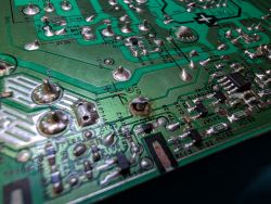 Close-up of a green PCB underside with solder joints, traces, and markings including “+” and “C17”.