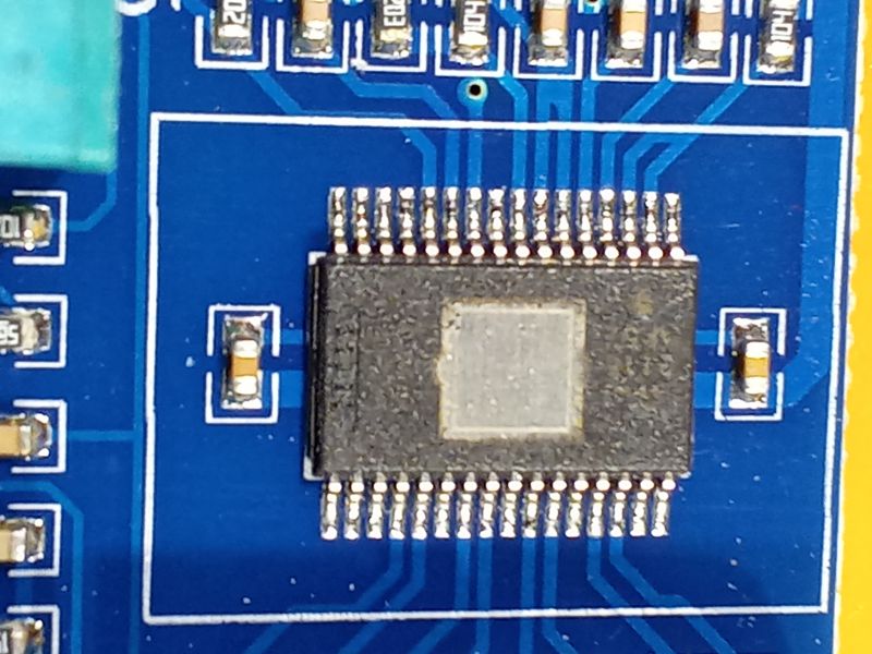 Mikrochip zamontowany na niebieskiej płytce drukowanej z widocznymi ścieżkami i komponentami.