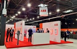 ABB trade fair booth with white walls, red carpet, and several people in suits.