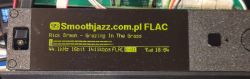 Green OLED display in a dark plexiglass enclosure showing FLAC audio information