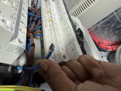 Zbliżenie na rękę trzymającą niezaizolowany, skręcany przewód miedziany przed podłączeniem do wyłącznika w rozdzielnicy elektrycznej.