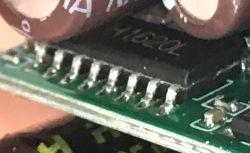 Macro of an SOIC integrated circuit on a green PCB, with soldered pins visible.
