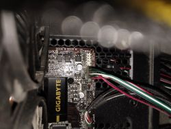 Zbliżenie wnętrza komputera z widoczną płytą główną marki Gigabyte i podłączonymi przewodami.