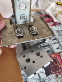 Zbliżenie na metalowy uchwyt z przykręconą wygiętą płytką i śrubami