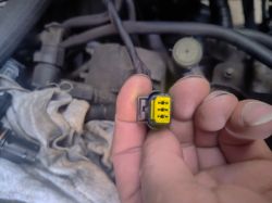 Dłoń trzyma żółtą wtyczkę elektryczną na tle komory silnika samochodu