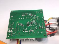 Spód zielonej płytki PCB z widocznymi ścieżkami, elementami SMD i lutowanymi połączeniami przewodów.