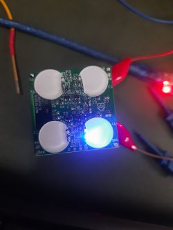Close-up of a PCB with four white capacitive touch sensors and a glowing blue LED.