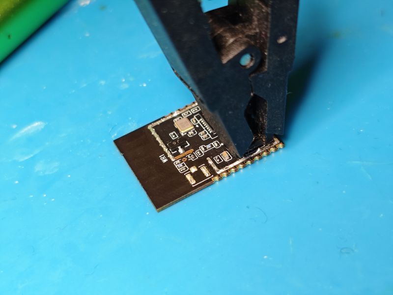 Small electronic module on a blue mat, held with tweezers; “WIFI” label visible.