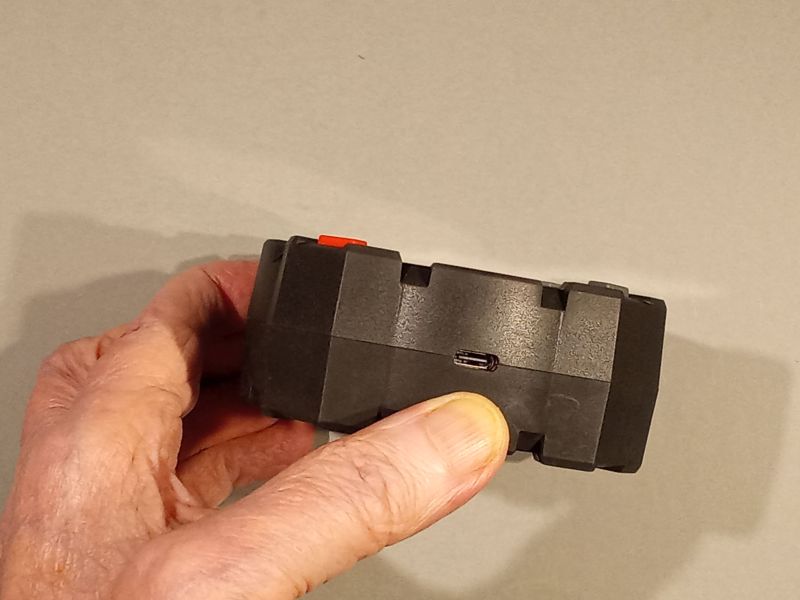 Dłoń trzyma czarne urządzenie z portem USB‑C, na jasnym tle