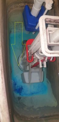 Wnętrze spłuczki WC z niebieskim zaworem i mechanizmem spustu; żółta strzałka wskazuje dolny element