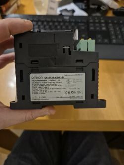 Sterownik programowalny Omron CP1H-XA40DT1-D trzymany w dłoni na tle biurka i klawiatury