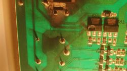 Uszkodzony fragment zielonej płytki PCB z przypalonymi ścieżkami oraz jednym nadpalonym elementem elektronicznym.