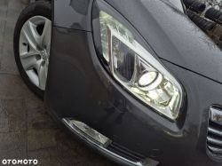 Left front headlight and bumper of a gray passenger car, visible alloy wheel and tire.