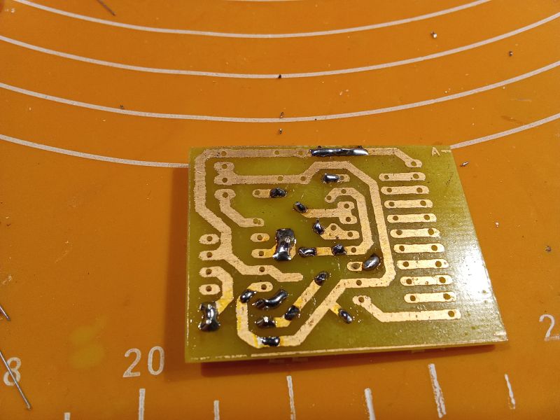 A printed circuit board with solder points on an orange mat.