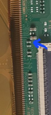 Zbliżenie na zieloną płytkę PCB z niebieską strzałką wskazującą na komponenty.