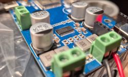 Close-up of a blue PCB with an IC chip, capacitors, and green screw terminals