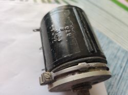Czarny cylindryczny element metalowy z uchwytem i śrubą, fotografowany z bliska.