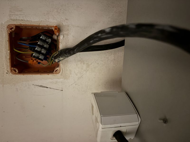 Otwarta puszka elektryczna z listwą zaciskową i przewodami oraz białe gniazdo z wpiętą wtyczką