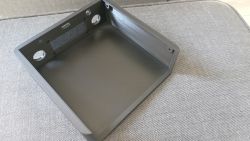 Czarna, plastikowa obudowa z wydrukiem 3D z widocznymi otworami montażowymi i technologicznymi, ustawiona na szarej kanapie.