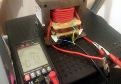 Transformator z mikrofali z nowym uzwojeniem i multimetrem w tle.