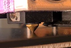 Side macro close-up of a 3D printer nozzle near the build plate