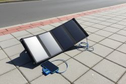 Solar panel on pavement next to a street, connected to a device via blue cable