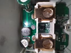 Top view of a printed circuit board with electronic components inside a device, featuring two large metal connectors and a capacitor.