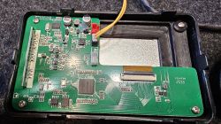 Zbliżenie na otwarty panel kontrolny z widoczną zieloną płytą drukowaną i podłączonymi kablami.