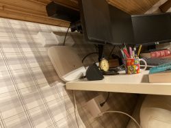 Biurko z monitorem, akcesoriami biurowymi, zegarem, kubkiem i urządzeniem sieciowym.