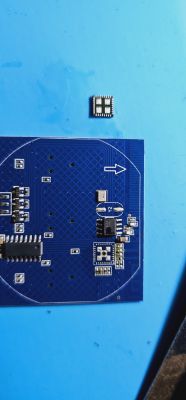 The image shows a blue printed circuit board with a detached SMD component next to it.