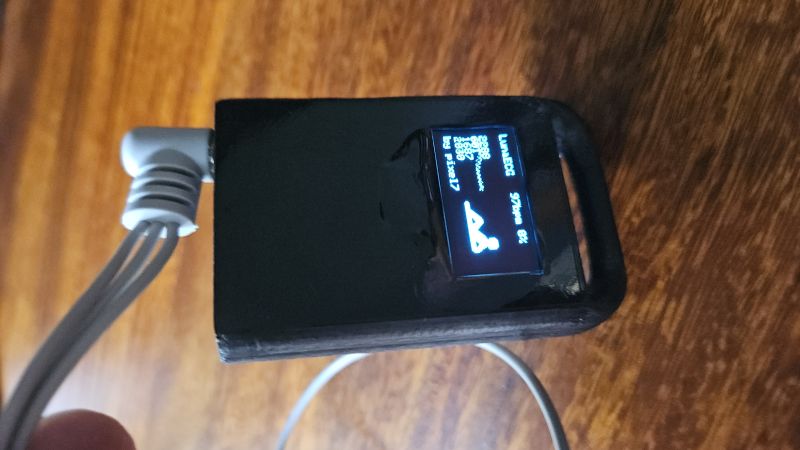 Małe czarne urządzenie z ekranem OLED pokazującym dane EKG i ikonę leżącej postaci