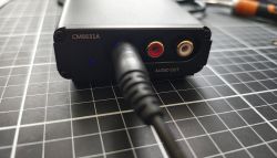 Przód aluminiowego DAC-a CM6631A z podłączonym wtykiem i wyjściami RCA „AUDIO OUT”