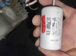 Ręka trzymająca biały kondensator KEMOT z oznaczeniami i etykietą Made in China.