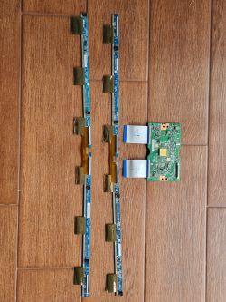 Cztery długie paski elektroniki i jedna płytka drukowana leżące na brązowej podłodze.