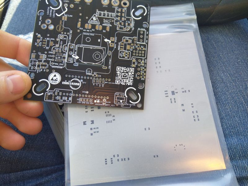 Close-up of a newly received printed circuit board (PCB) held in hand, with other PCBs in transparent packaging in the background.