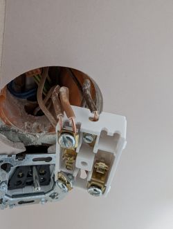 Widok zbliżeniowy na instalację elektryczną z wystającymi przewodami i otwartym wyłącznikiem.