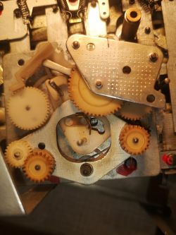 Widok zbliżeniowy na mechanizm zębatkowy z metalową płytką i sprężynami.