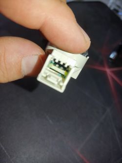 Zbliżenie na plastikową wtyczkę z odsłoniętymi stykami, trzymaną w palcach.