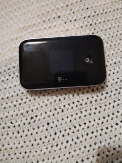 Czarny przenośny router T-Mobile z przyciskiem zasilania na tle dzianiny