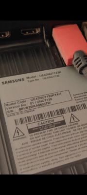 Naklejka informacyjna z tyłu telewizora Samsung UE43NU7122KXXH z widocznym portem HDMI i przewodami.
