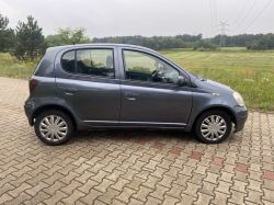 A grey hatchback car parked on a brick pavement by a green field.
