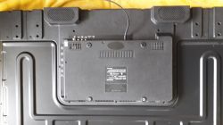Back of a TV with ports and a label visible, lying on yellow fabric.