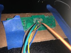 Close-up of a circuit board with connected colorful wires and secured with blue tape.