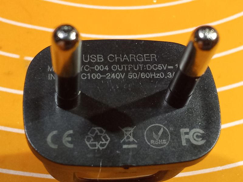 Zbliżenie na czarną ładowarkę USB z wtyczką do gniazda 230V i oznaczeniami technicznymi.