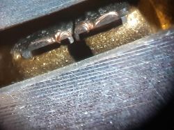Zbliżenie elementu elektronicznego sfotografowanego przez mikroskop, widoczne dwie miedziane ścieżki i metalowa powierzchnia.